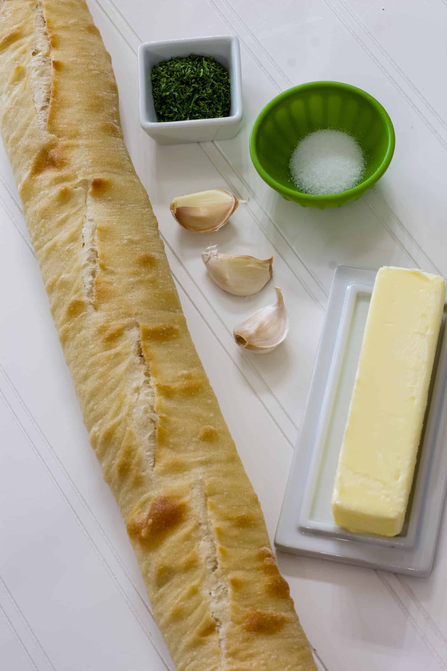 The baguette, butter, garlic, parsley and salt in individual portions on a white background.