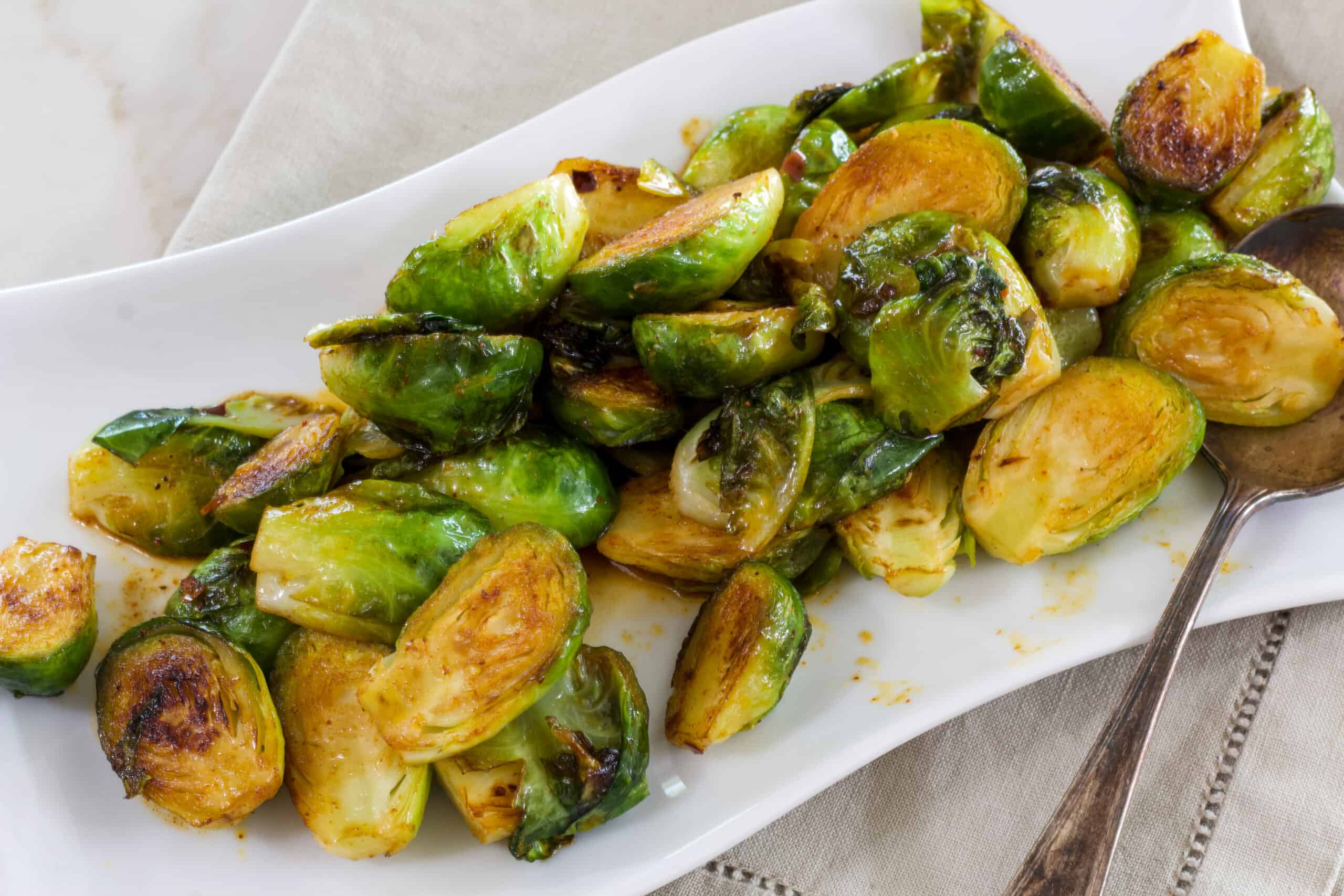 A white serving plate with copycat longhorn brussels sprouts on it.