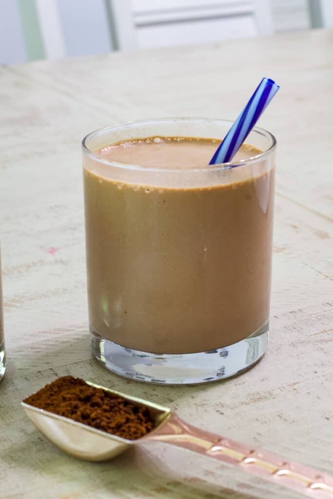 A smoothie and a copper tablespoon filled with instant dark roast coffee in the foreground.