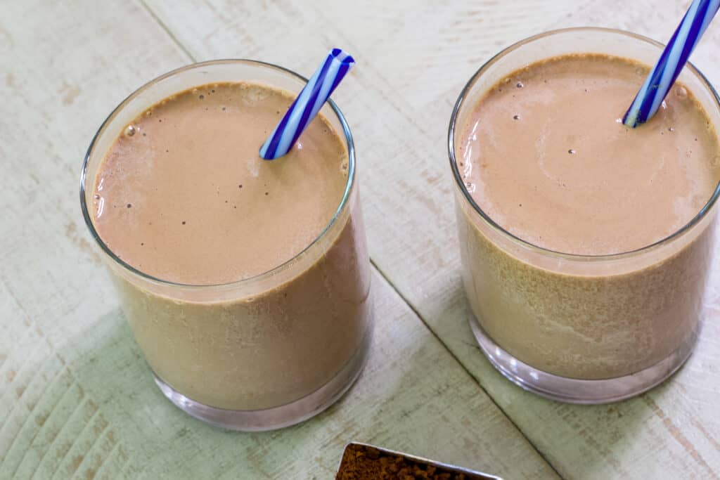 The top view of two glass tumblers filled with mocha madness smoothie, they have blue striped straws in them.