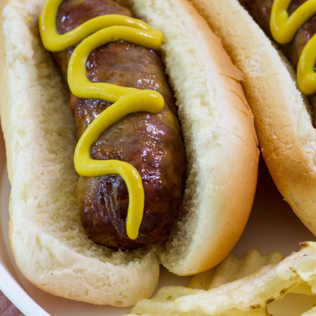 Close up of one cheddar bratwurst in a hot dog bun with mustard on it.