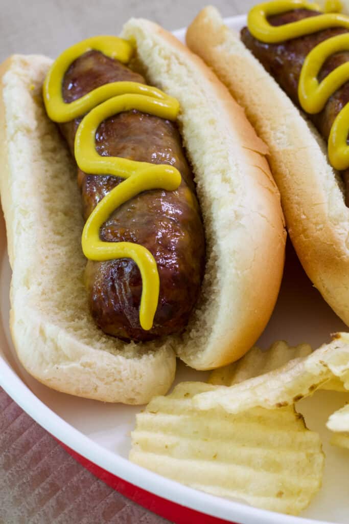 One cheddar brats in a hot dog bun with potato chips on the side.