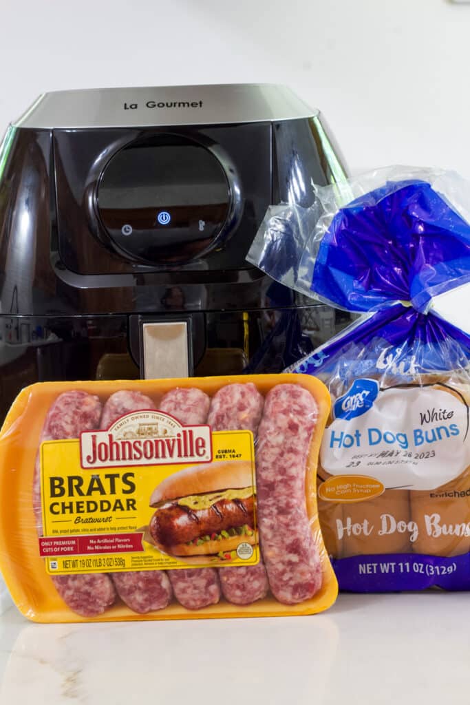 One package of Johnsonville cheddar brats and one package of great value hot dog buns sitting in front of an air fryer.