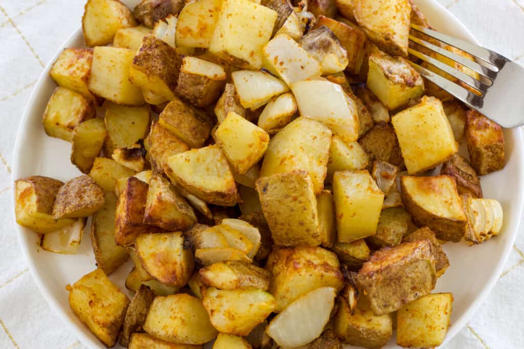 A plate with potatoes and onions and a fork on the right side.
