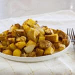 The plate of potatoes and onions on a white and gold napkin with a silver fork on the right side.