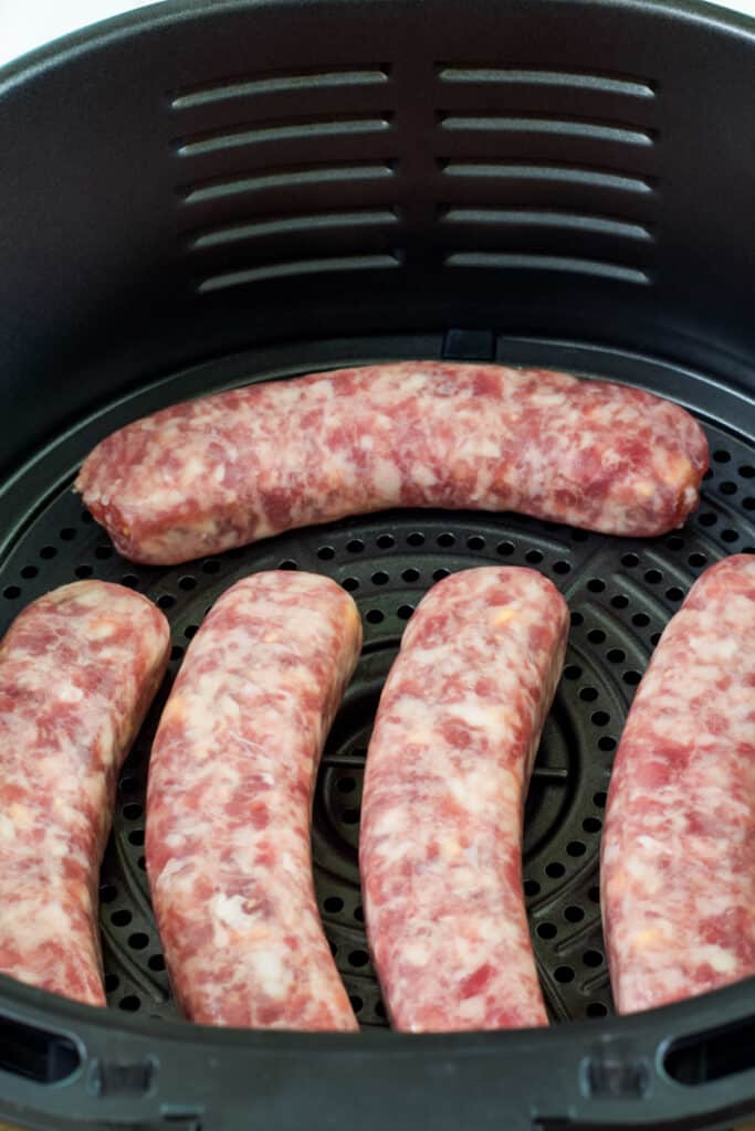 Five cheddar brats in the basket of an air fryer before they are cooked.