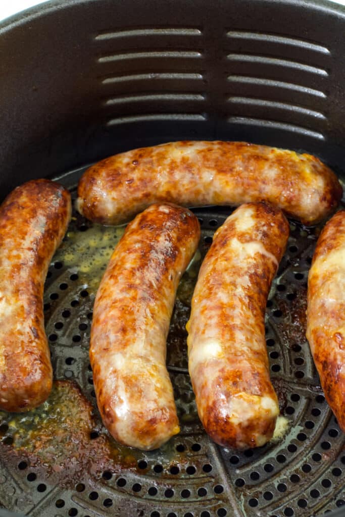 Five cheddar brats in the basket of the air fryer after they were air fried.