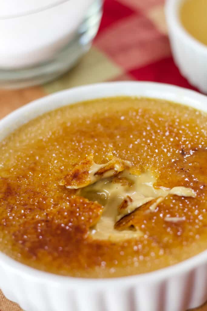 A ramekin of coffee creme brulee that has the caramelized sugar topping cracked so you can see the custard under it.