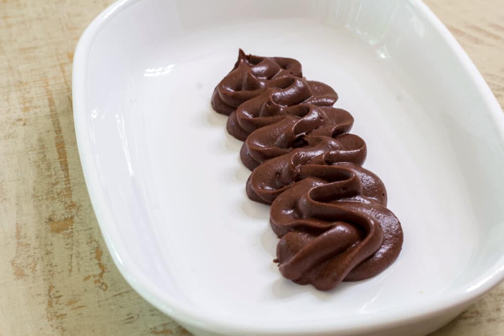 A line of frosting chocolate frosting piped onto a white plate.