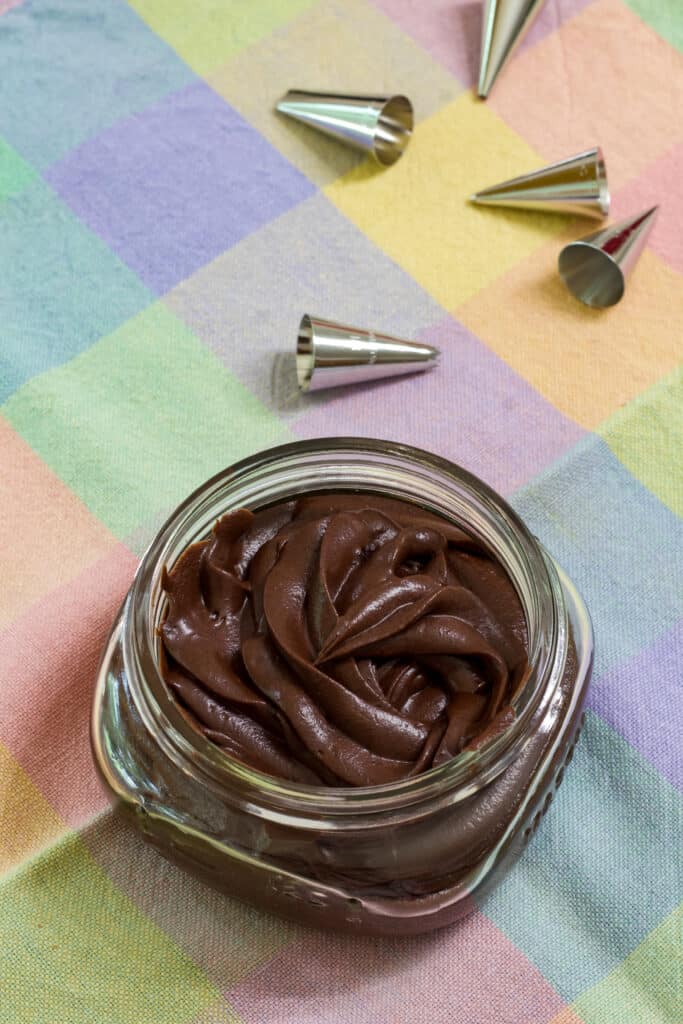 A small mason jar with chocolate frosting piped into it sitting on a pastel checkered napkin.