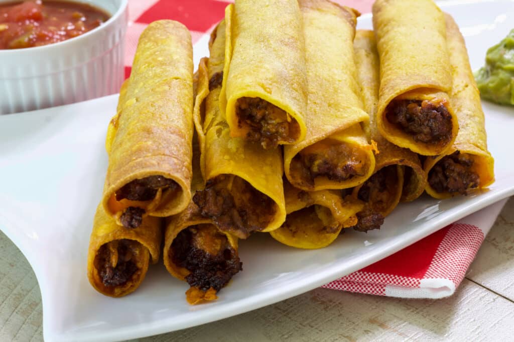 Nine taquitos on a plate showing the meat and cheese inside.