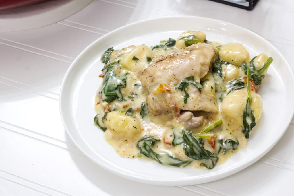 One serving of creamy chicken and gnocchi on a white plate.