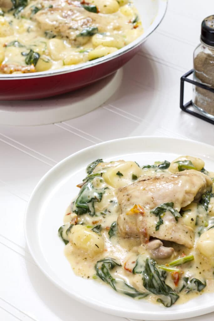 One serving of creamy chicken and gnocchi in the foreground and the skillet with the other servings in the back ground.