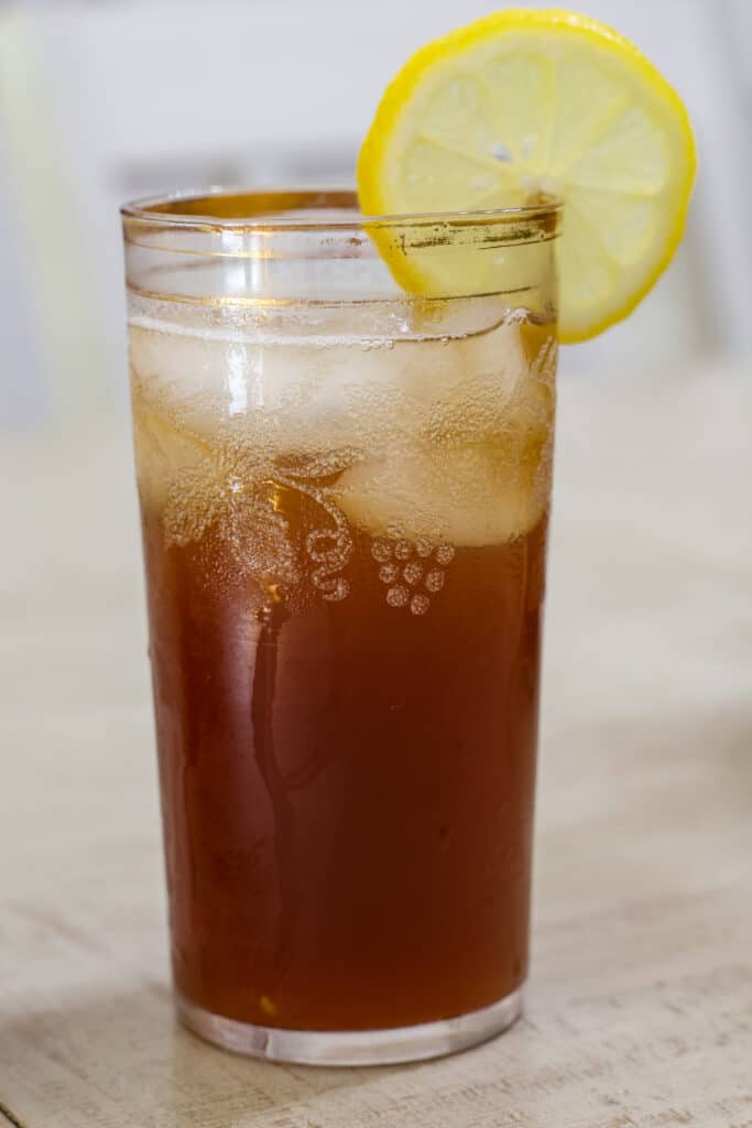 One glass of The Best Luzianne Southern Sweet Iced Tea with a lemon slice on the rim of the glass sitting on a table.