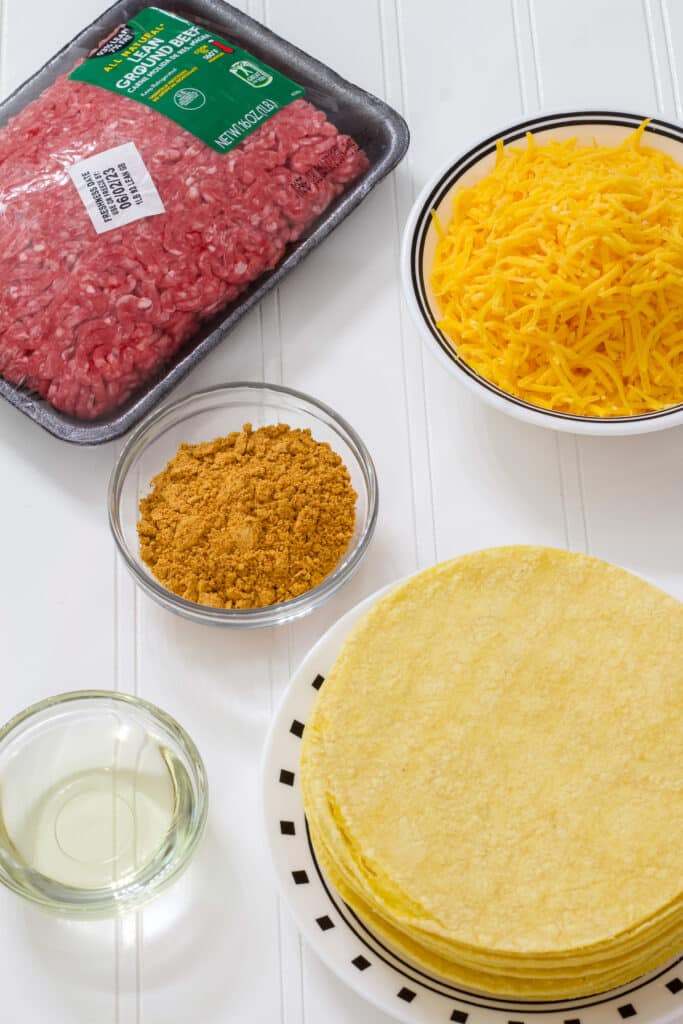 The raw ground beef, corn tortillas, shredded cheese, taco seasoning and canola oil portioned out.
