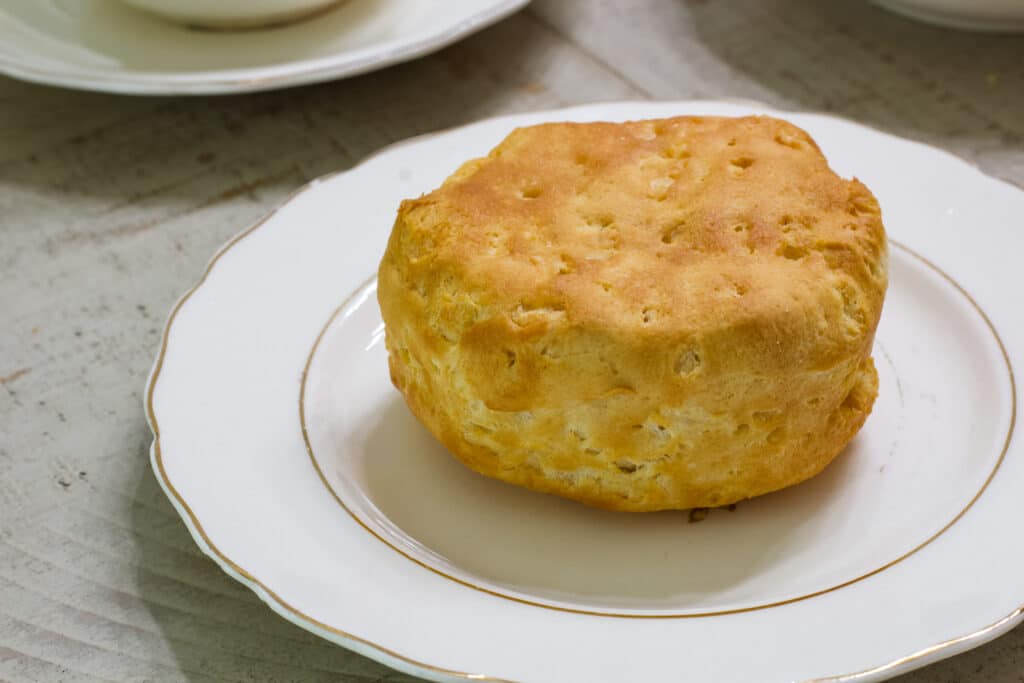 One whole air fried canned pillsbury biscuit on a cream colored china plate.