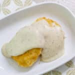 overhead view of white gravy on a biscuit on a white plate.