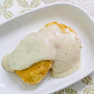 overhead view of white gravy on a biscuit on a white plate.