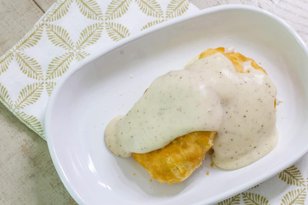 Easy Homemade Southern White Country Gravy over a biscuit on a white plate.