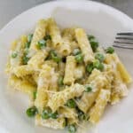 Overhead close up of one serving of lemon pasta with peas and ricotta on a white plate.