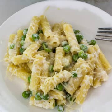 Overhead close up of one serving of lemon pasta with peas and ricotta on a white plate.
