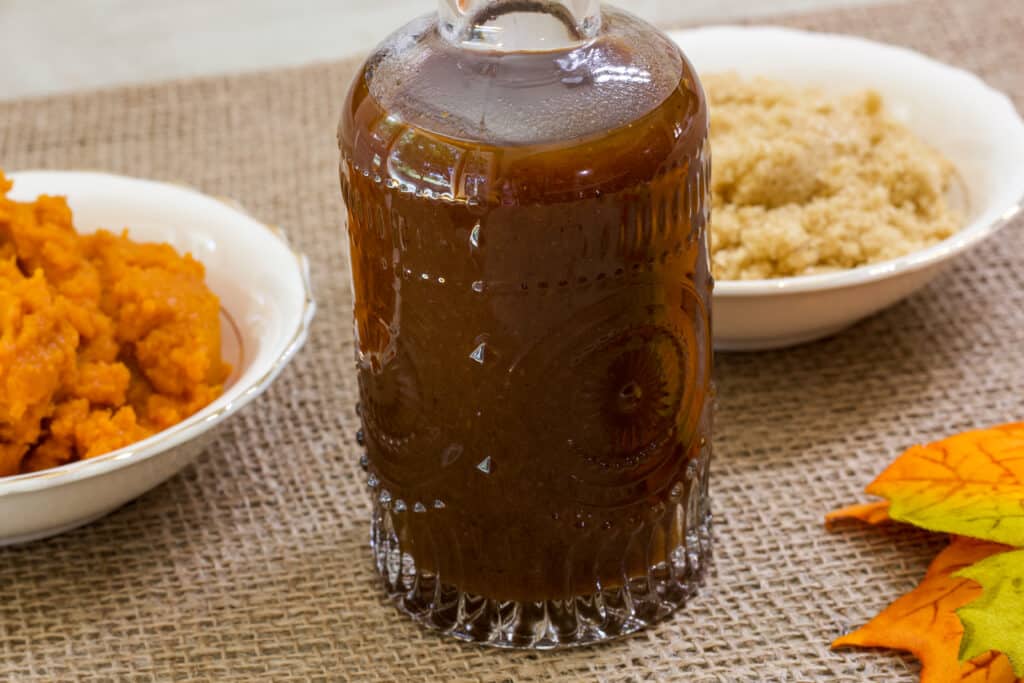A jar of coffee syrup and a small bowl with pumpkin puree and a small bowl of brown sugar sitting on a piece of burlap.