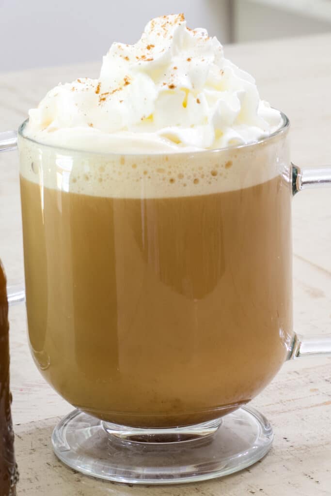 A cup of pumpkin spice coffee topped with whipped cream in a glass mug.
