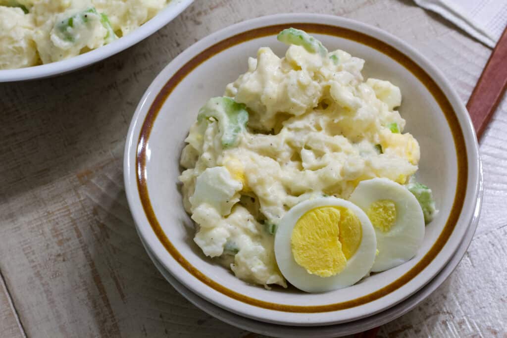 A small bowl of potato salad that has 2 slices of hard cooked eggs on the bottom center.