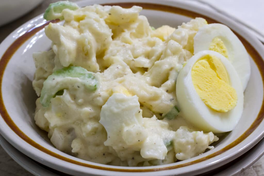 One serving of potato salad in a small bowl with 2 slices of hard boiled egg on the right side.