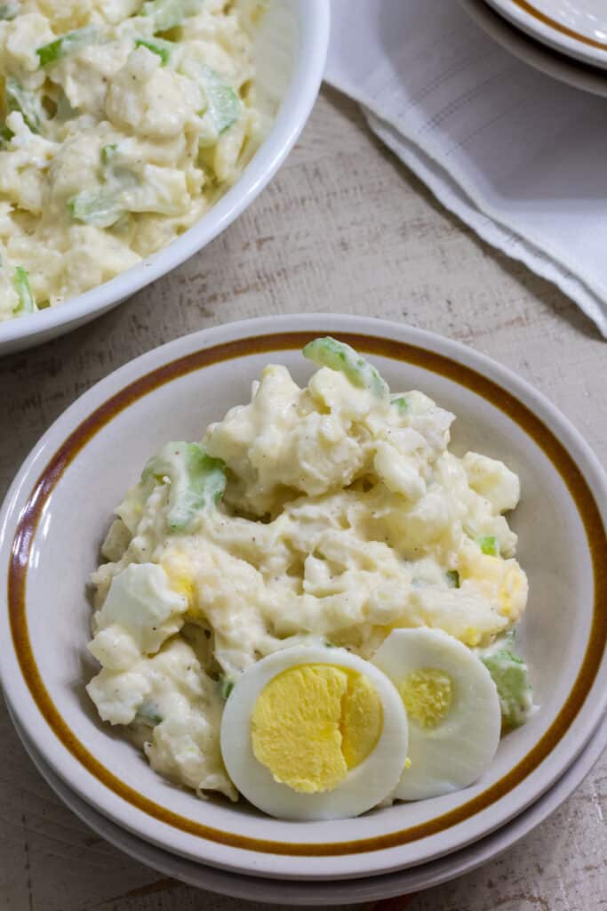 A small bowl with one serving of potato salad and just the corner of a large bowl in the background.