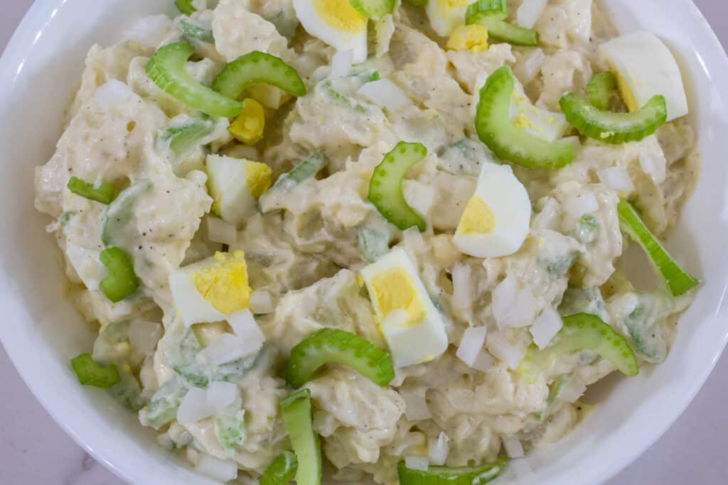 Overhead view of a bowl of potato salad with pieces of celery, cooked egg and onion that hasn't been mixed in.