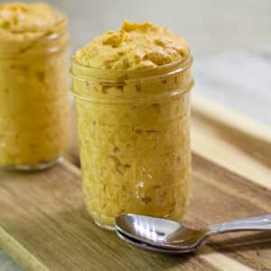 A jar of pumpkin fluff and two spoons in the foreground and another jar in the background.