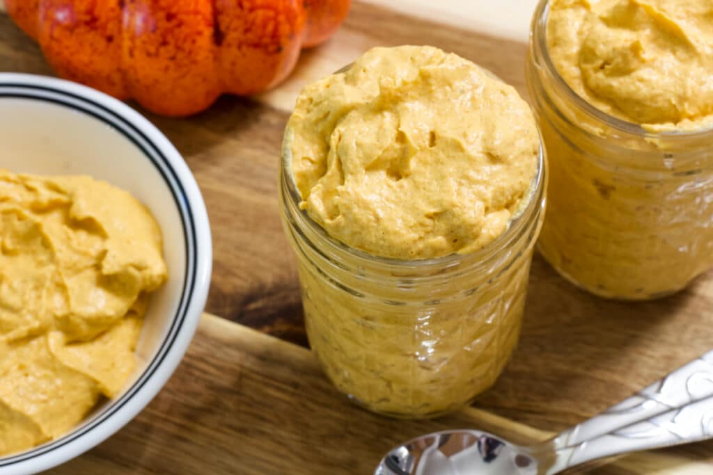 Two small mason jars and a small white bowl filled with Low Calorie Weight Watchers Pumpkin Fluff.