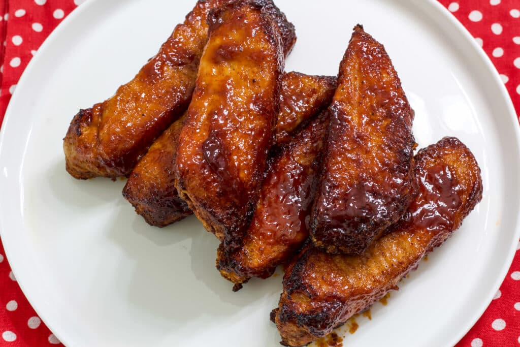 Overhead view of six ribs on a white plate that is sitting on a red and white napkin.