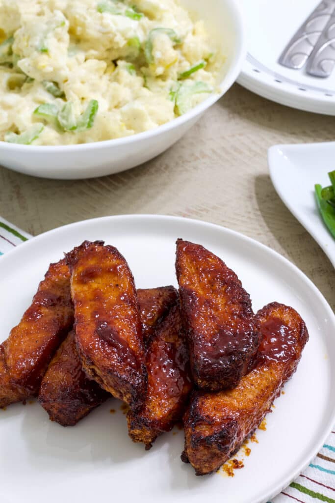 A plate of ribs in the at the bottom of the image and you can see part of a bowl of potato salad at the top of the image.