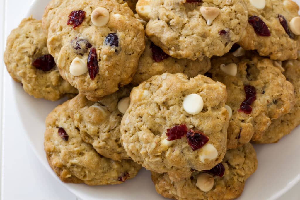 Several Soft Oatmeal White Chocolate Chip Cranberry Cookies piled on a white plate.