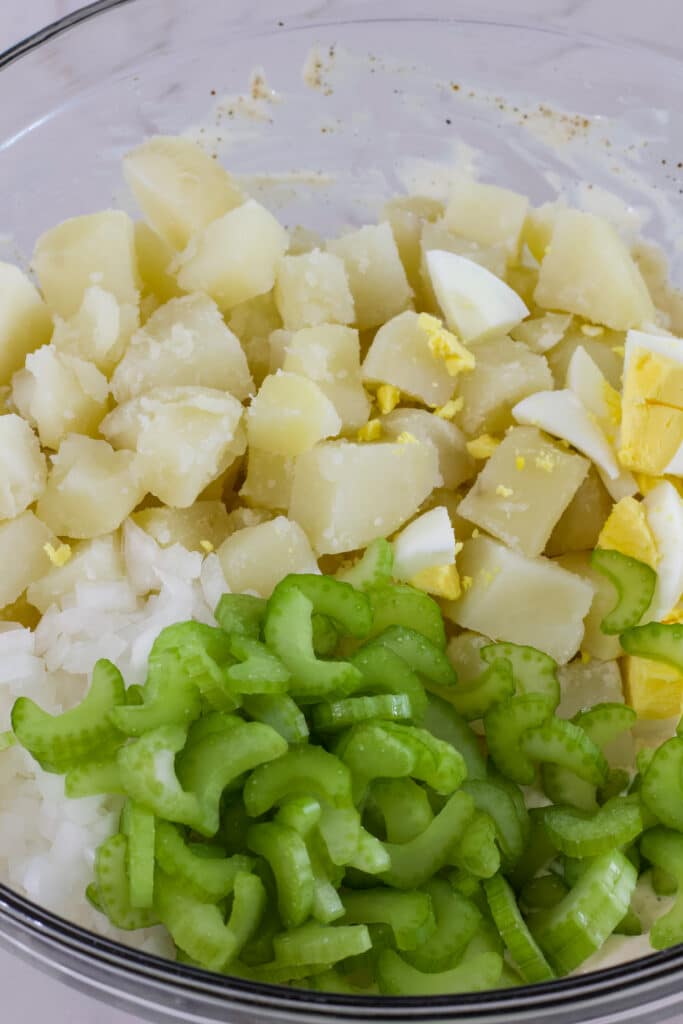 The cut up potatoes, celery onion and eggs in a large glass mixing bowl.