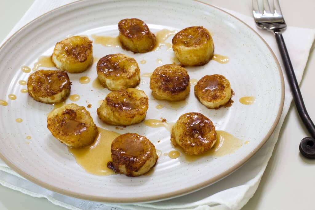 Many air fried banana coins on a plate drizzled with caramel sauce.