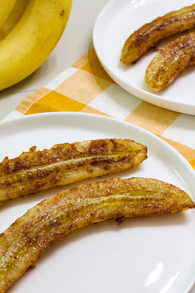 Two banana halves that have been air fried on a white plate.