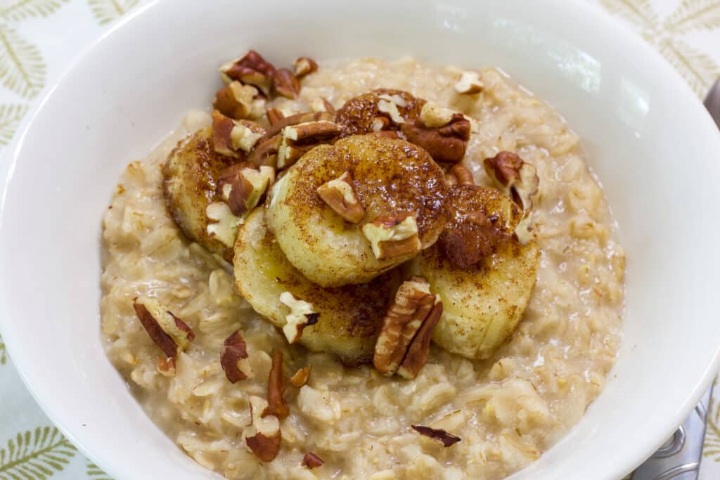 A white bow full of oatmeal that is topped with air fryer banana slices and chopped pecans.