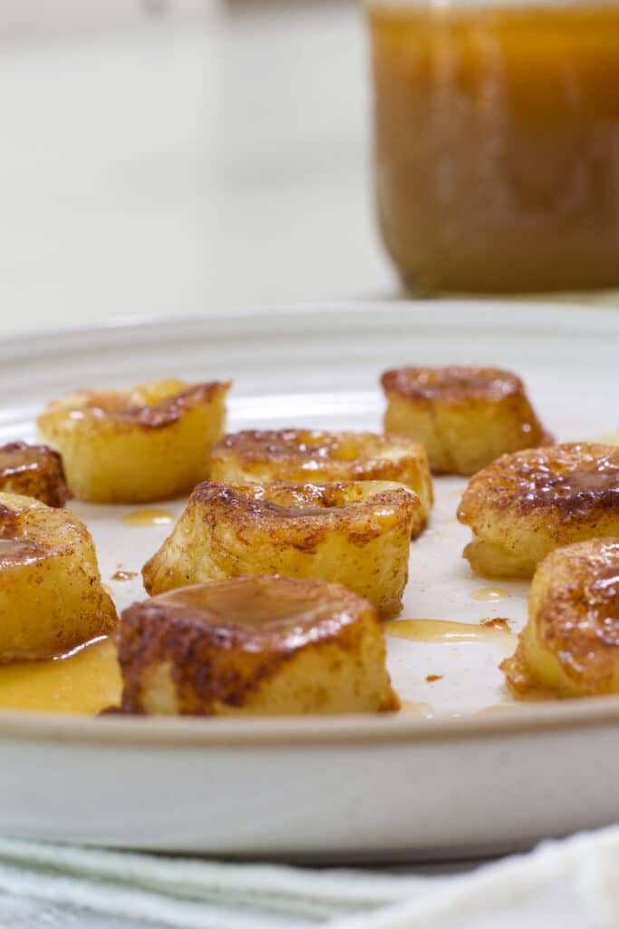 Close up side view of air fried banana slices drizzled with caramel sauce on a white plate.