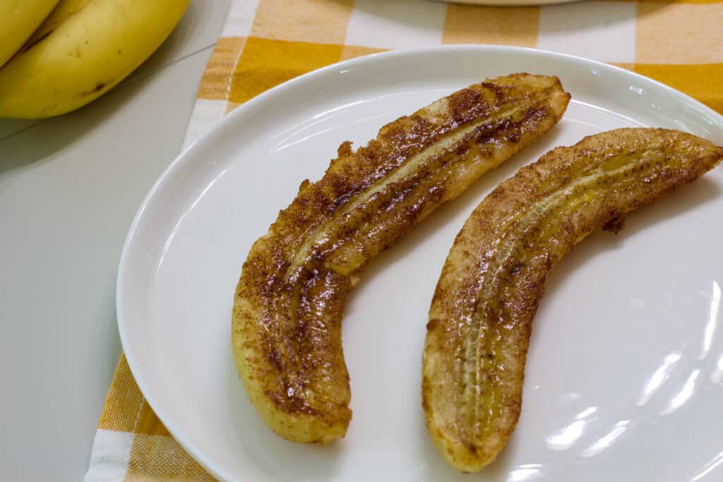 One banana that has been cut in half and air fried sitting on a white plate.