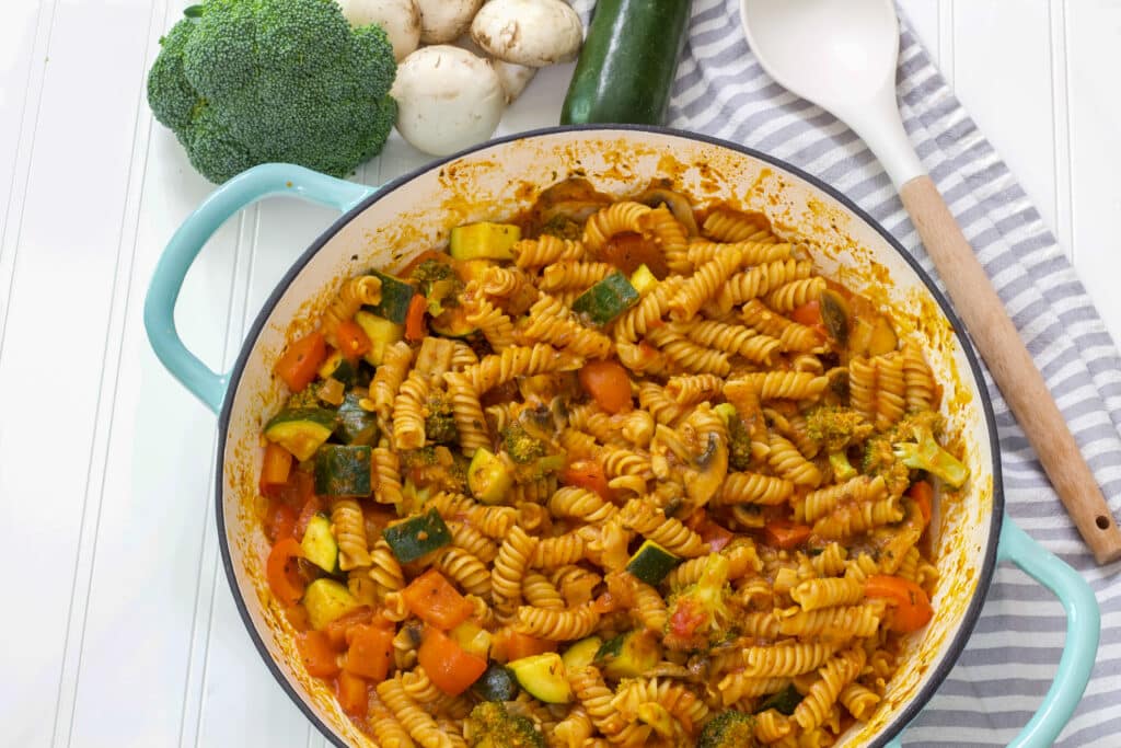 A pan full of vegetarian pasta and some vegetable and a wooden spoon sitting near it.