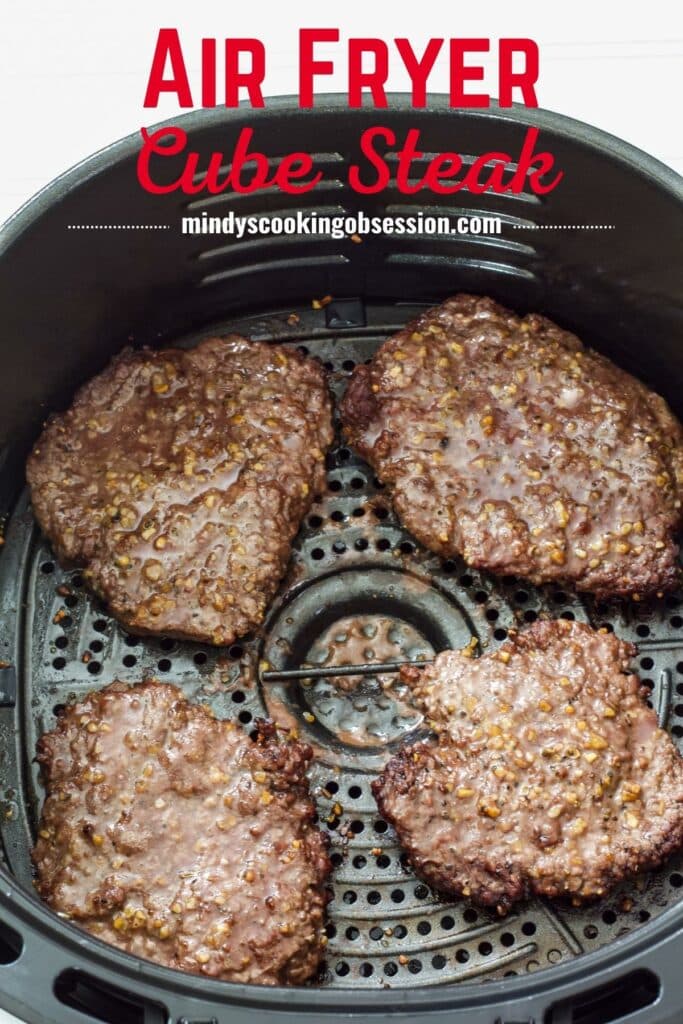 Four cooked cube steaks in the basket of the air fryer with the recipe title above it in text.