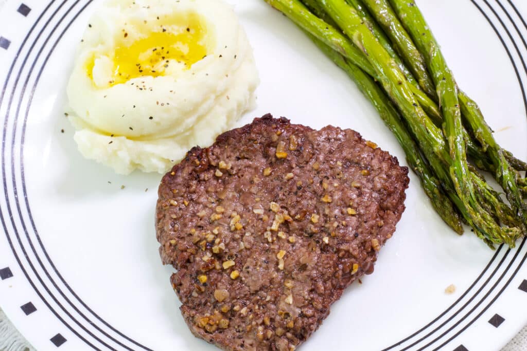 A plate with an air fried cube steak, serving of mashed potatoes and asparagus spears on it.