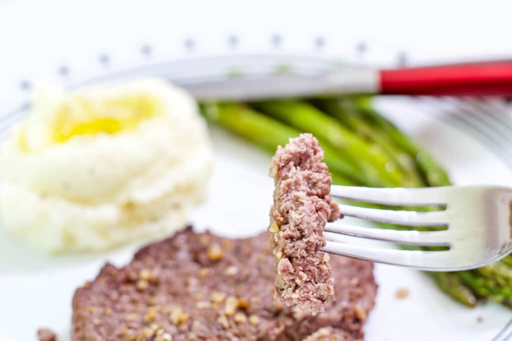 One piece of cooked cube steak on a fork exposing the very slightly pink center.