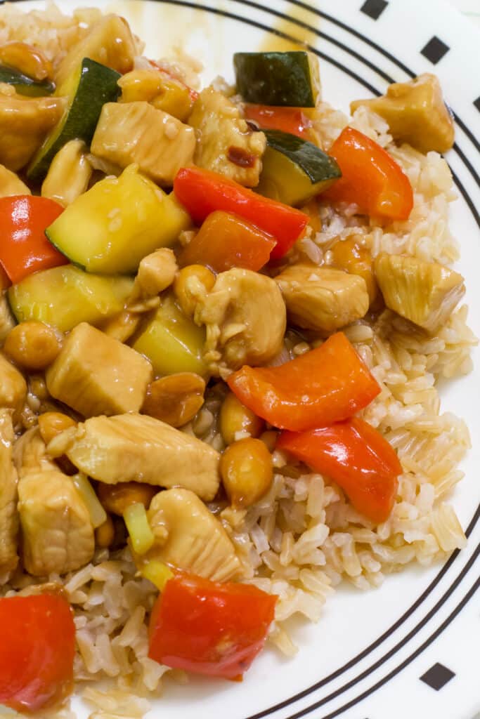 Overhead shot of the left half of a plate with one serving of kung pao chicken over brown rice.