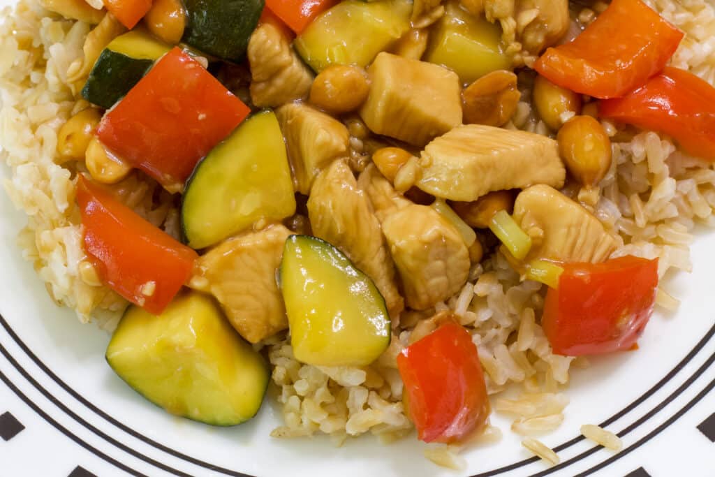 The bottom half of a plate of kung pao chicken on a bed of brown rice.