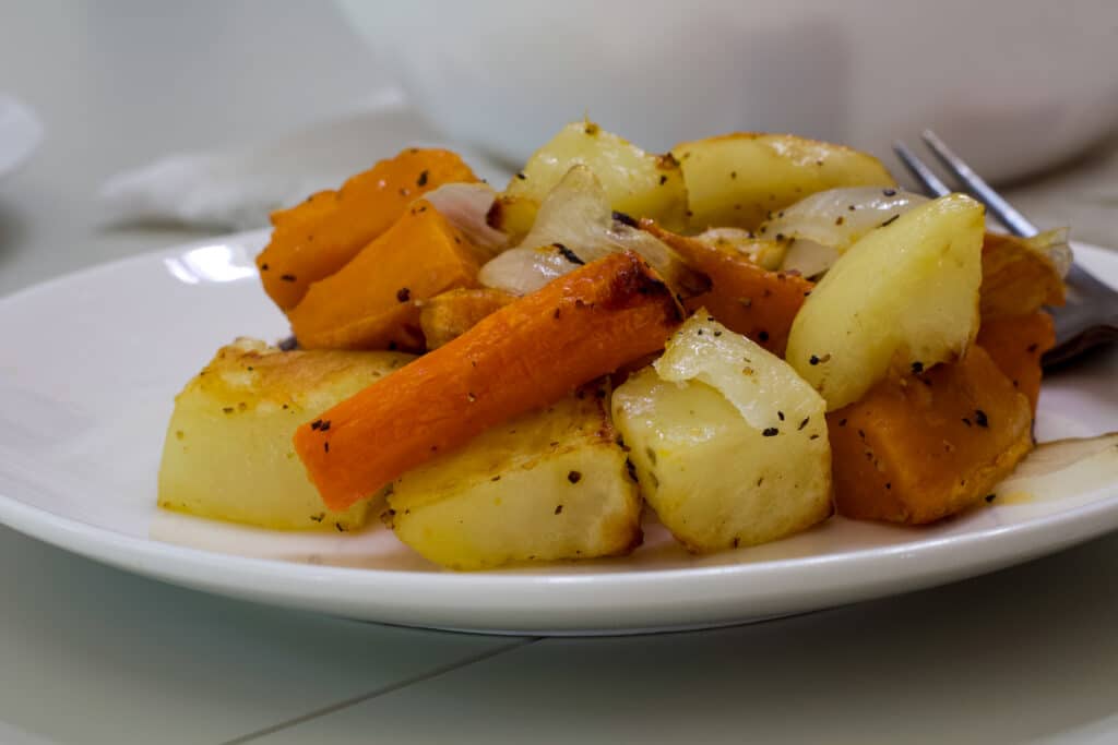 A close up shot from the side of one serving of roasted vegetables on a white plate.