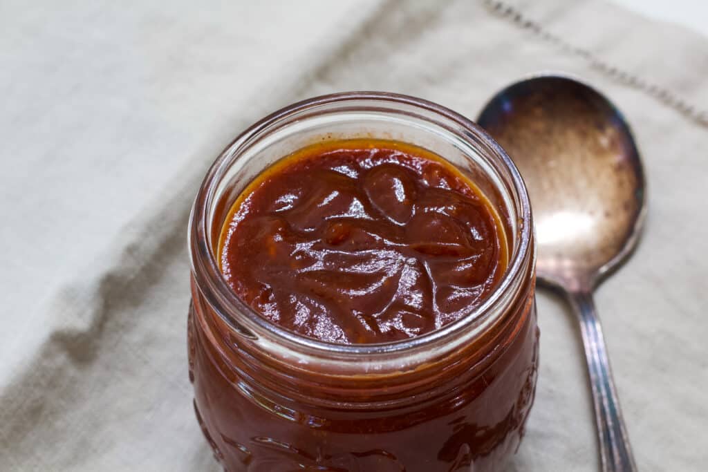 A jar of homemade chili sauce and an old silver soup spoon sitting next to it.